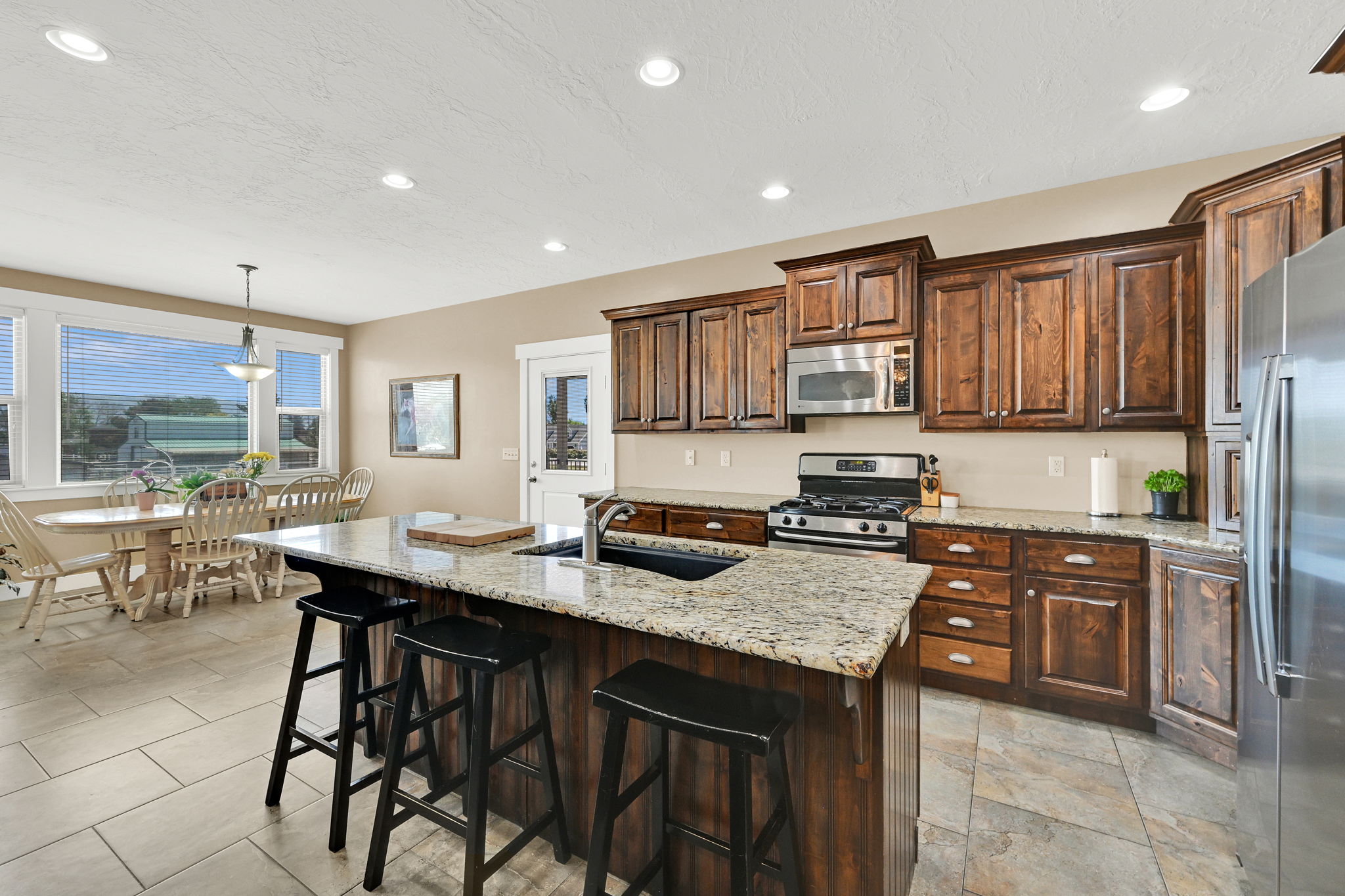 Kitchen featuring granite-topped island with integrated sink, stainless steel appliances, wood cabinetry, and recessed lighting
