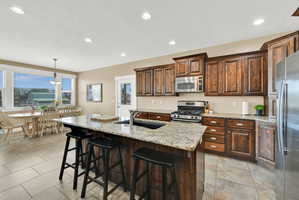 Kitchen featuring granite-topped island with integrated sink, stainless steel appliances, wood cabinetry, and recessed lighting