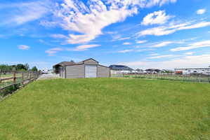 Expansive green lawn area featuring a split-rail fence, a metal outbuilding with an overhead door, and a covered patio structure