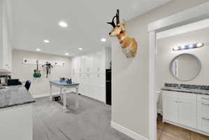 Spacious multi-purpose room featuring extensive built-in white cabinetry, recessed lighting, and grey carpeted flooring