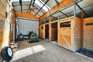 Interior structure featuring wood paneling, multiple barn-style stalls with sliding doors, a roll-up garage door, an exposed metal truss ceiling, and translucent roof panels
