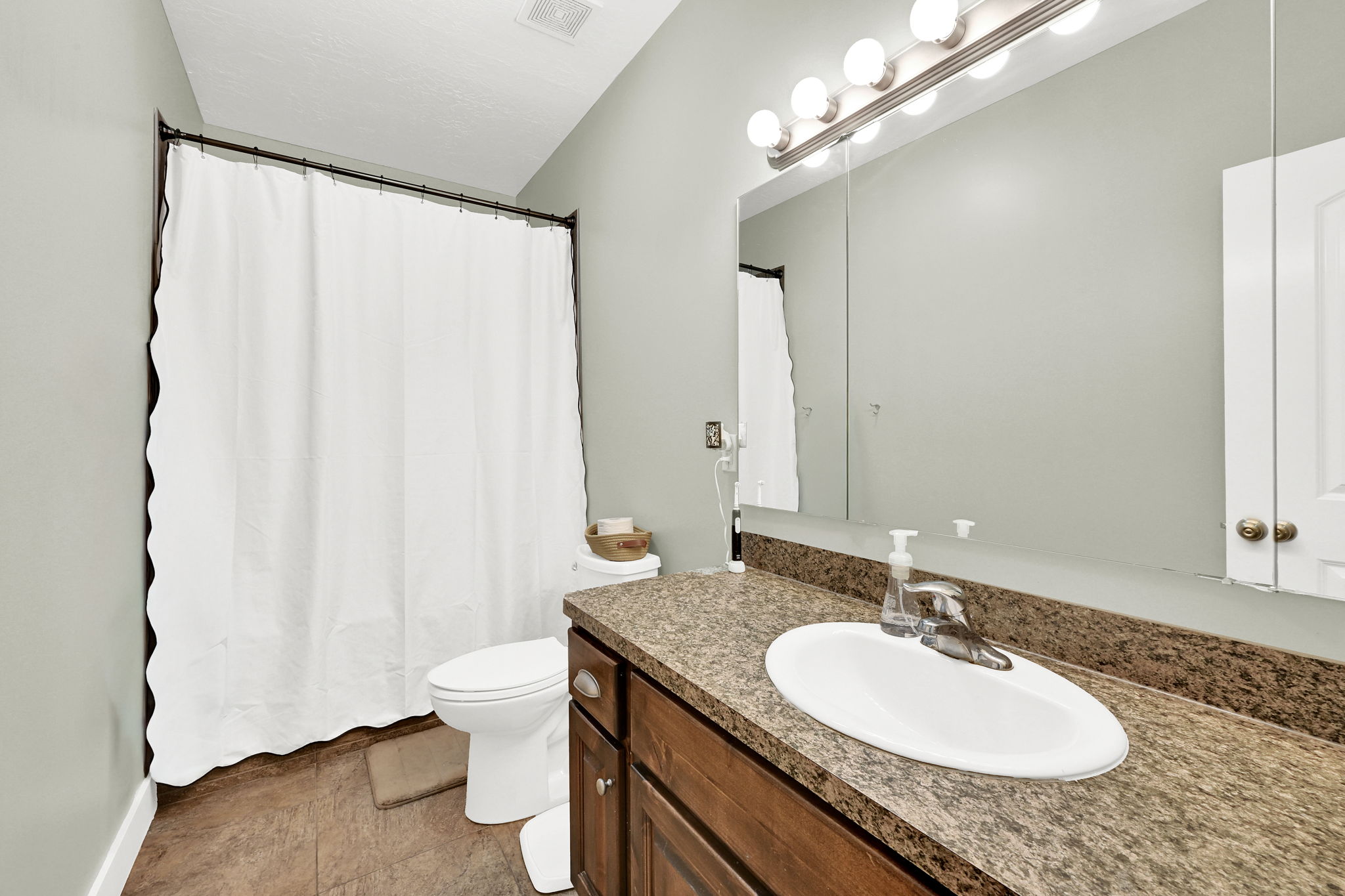 Bathroom featuring a single vanity with a laminate countertop, an oval undermount sink, and a large wall mirror with a six-bulb vanity light fixture