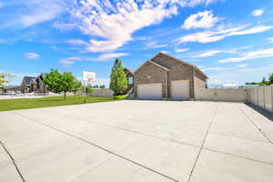 Expansive concrete driveway with a basketball hoop, brick exterior, two-car garage, and solid perimeter fencing
