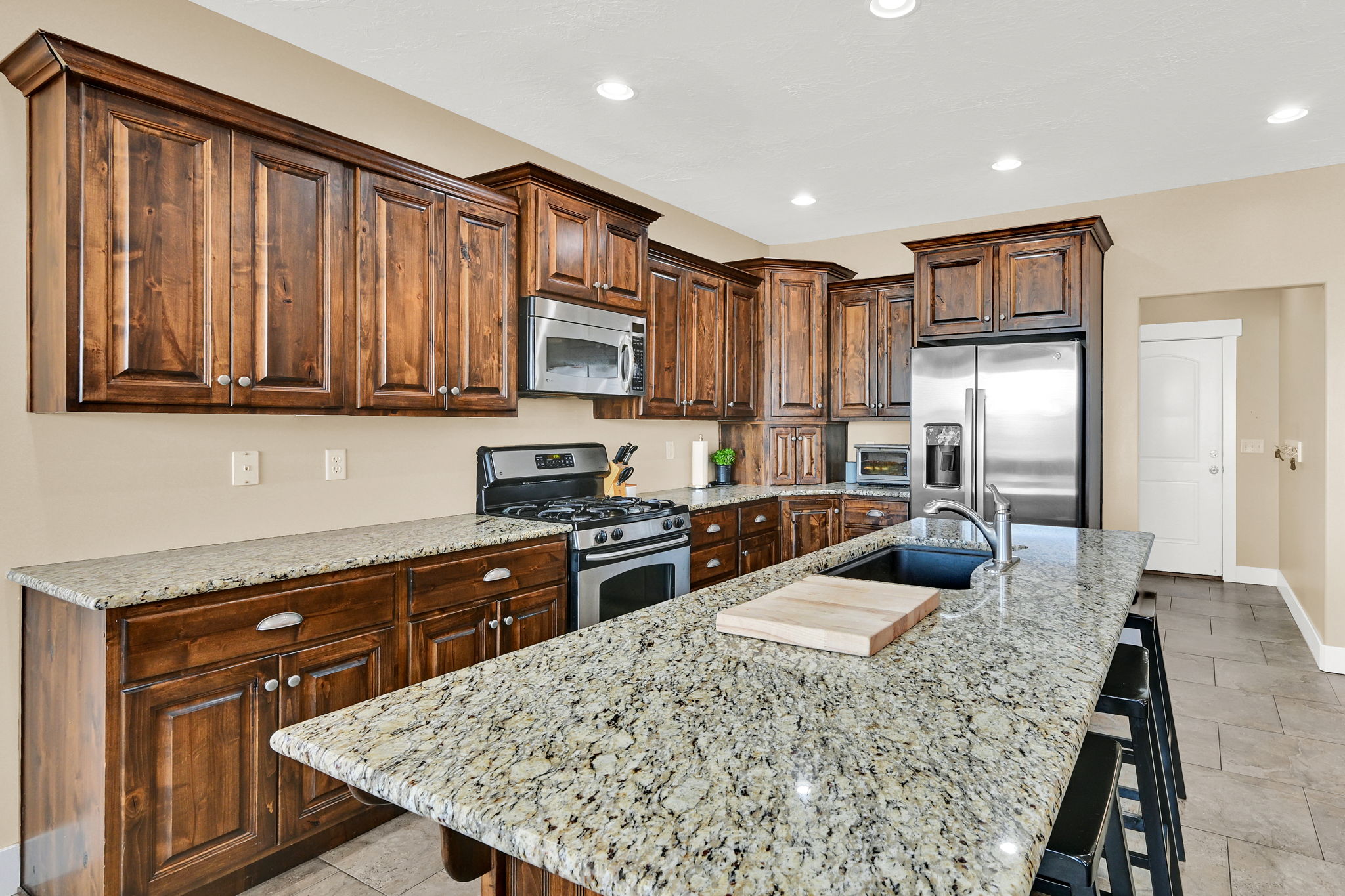 Kitchen featuring wood cabinetry, granite countertops, stainless steel appliances, a center island with a sink, and recessed lighting