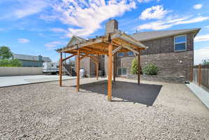 Spacious backyard featuring a wood pergola, gravel ground cover, brick exterior, stone retaining wall, and concrete pad