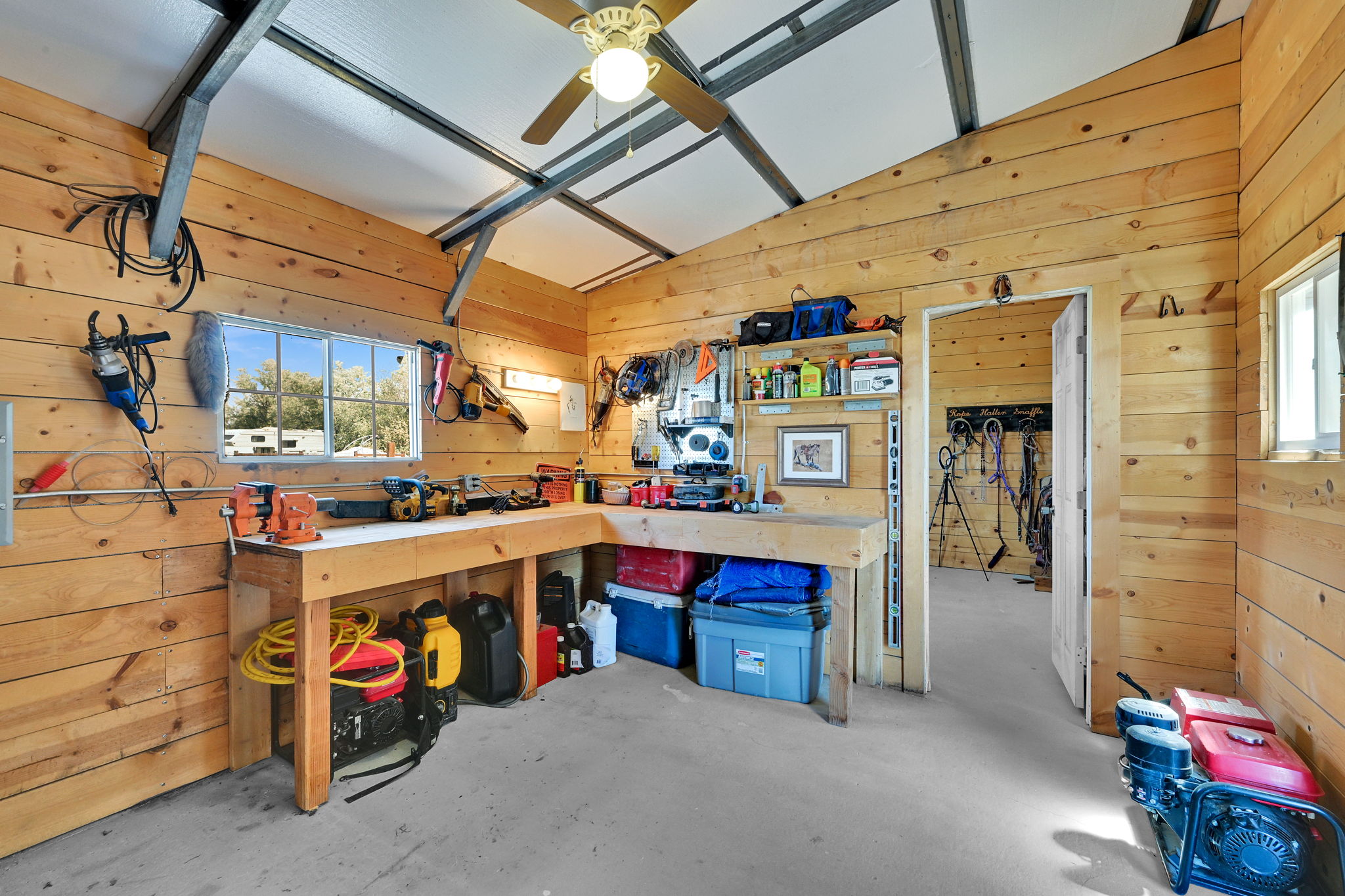 Spacious workshop featuring natural wood plank walls, exposed metal ceiling beams, a built-in workbench, and concrete flooring