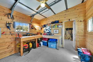 Spacious workshop featuring natural wood plank walls, exposed metal ceiling beams, a built-in workbench, and concrete flooring