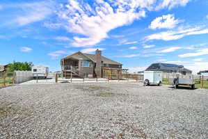 Expansive gravel yard area with a brick exterior structure featuring multiple windows, a second-story wooden deck with railing, and a ground-level patio with a wooden pergola