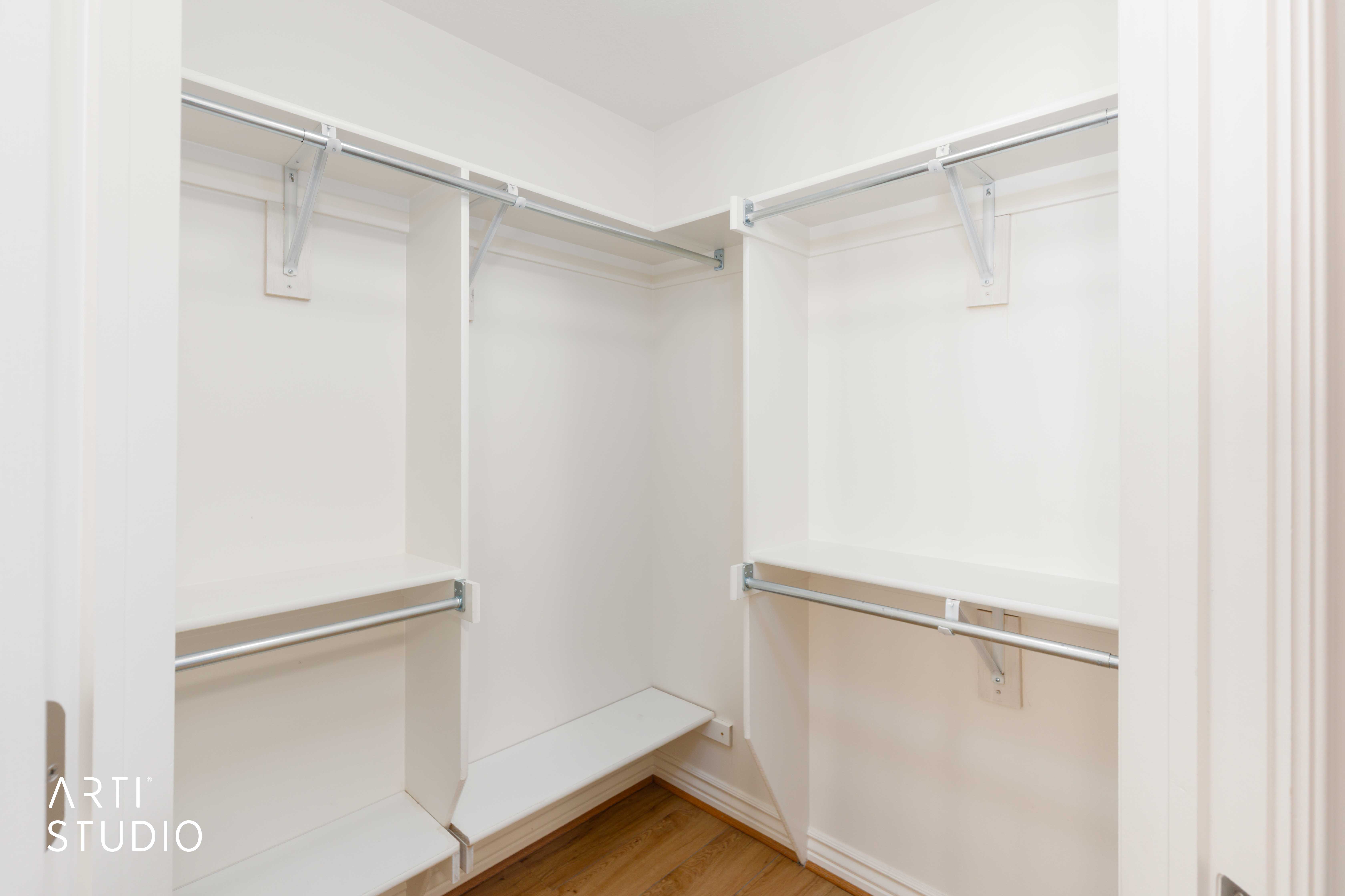 Walk-in closet with white shelving, multiple hanging rods, and wood-finish flooring