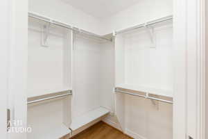 Walk-in closet with white shelving, multiple hanging rods, and wood-finish flooring
