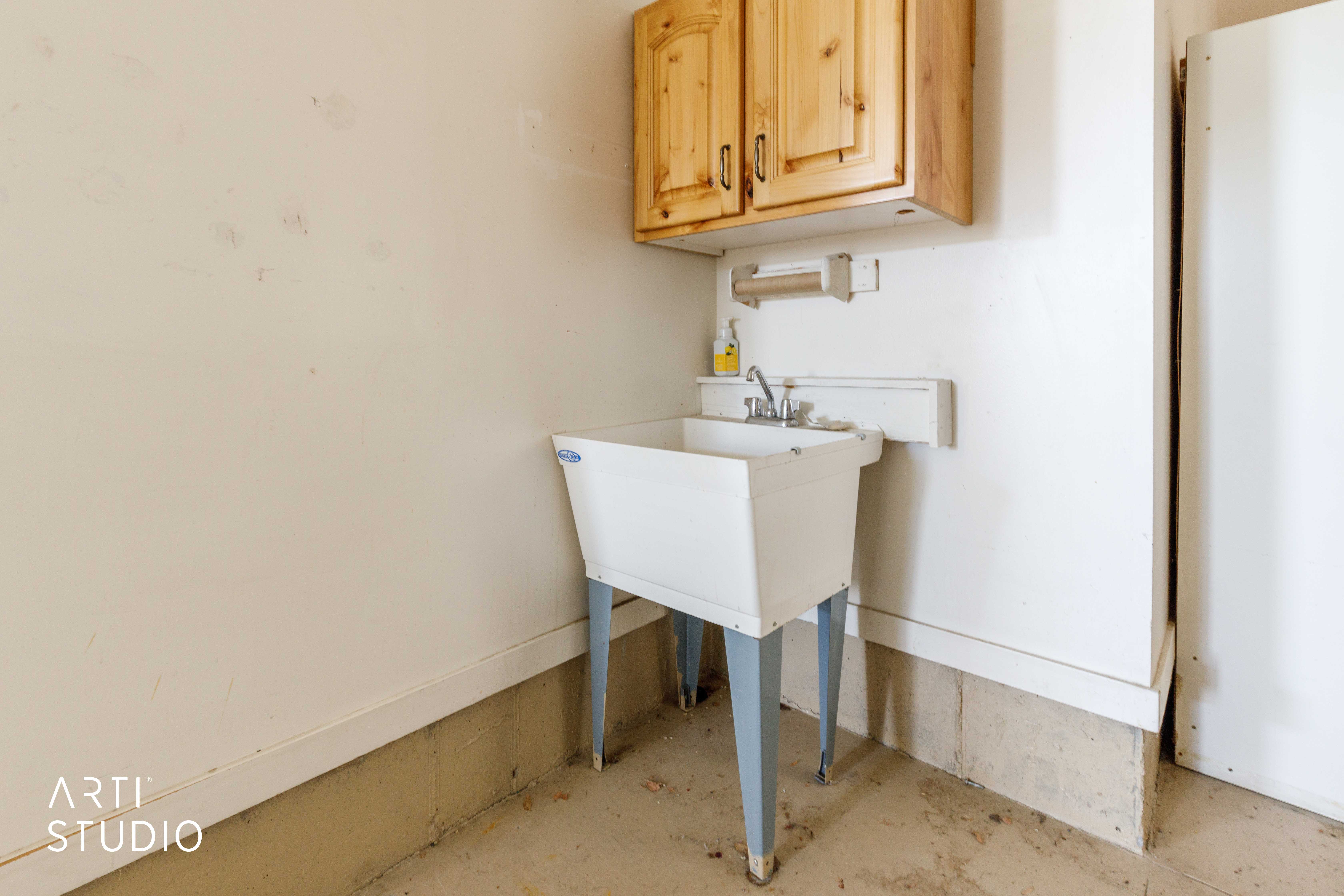 Utility sink area featuring a white basin with metal legs, chrome faucet, and overhead wood cabinetry