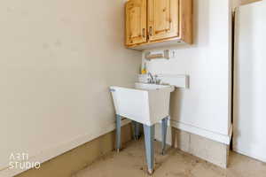 Utility sink area featuring a white basin with metal legs, chrome faucet, and overhead wood cabinetry