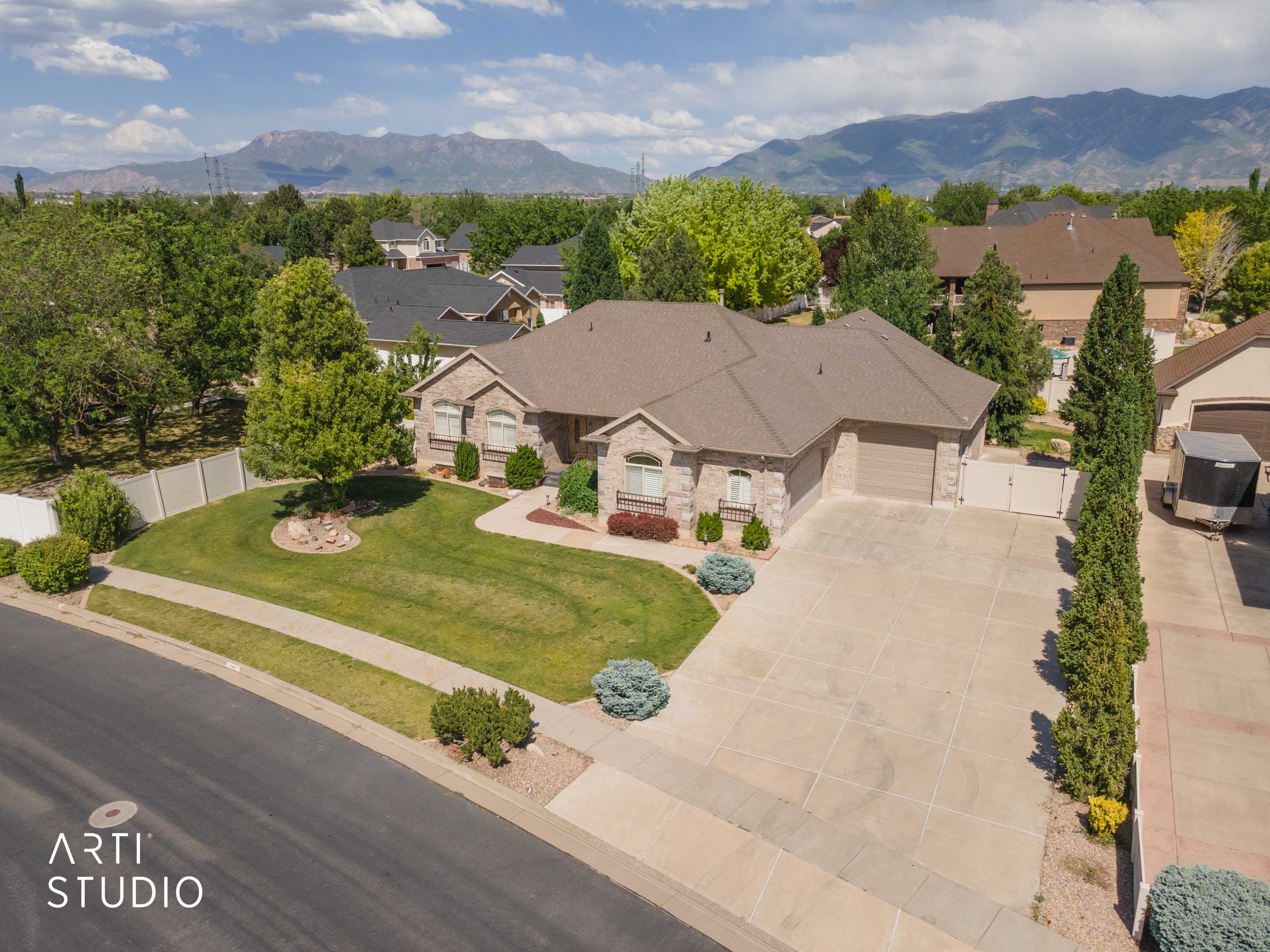 Expansive property featuring a stone and brick facade, a multi-car driveway, a two-car garage, mature landscaping, and a mountain backdrop