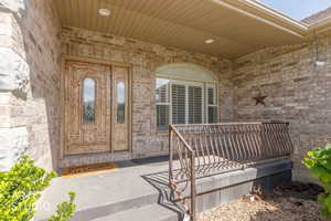 Brick exterior with a covered porch featuring a decorative wood-paneled door with glass inserts, an arched window with plantation shutters, and an ornate metal railing
