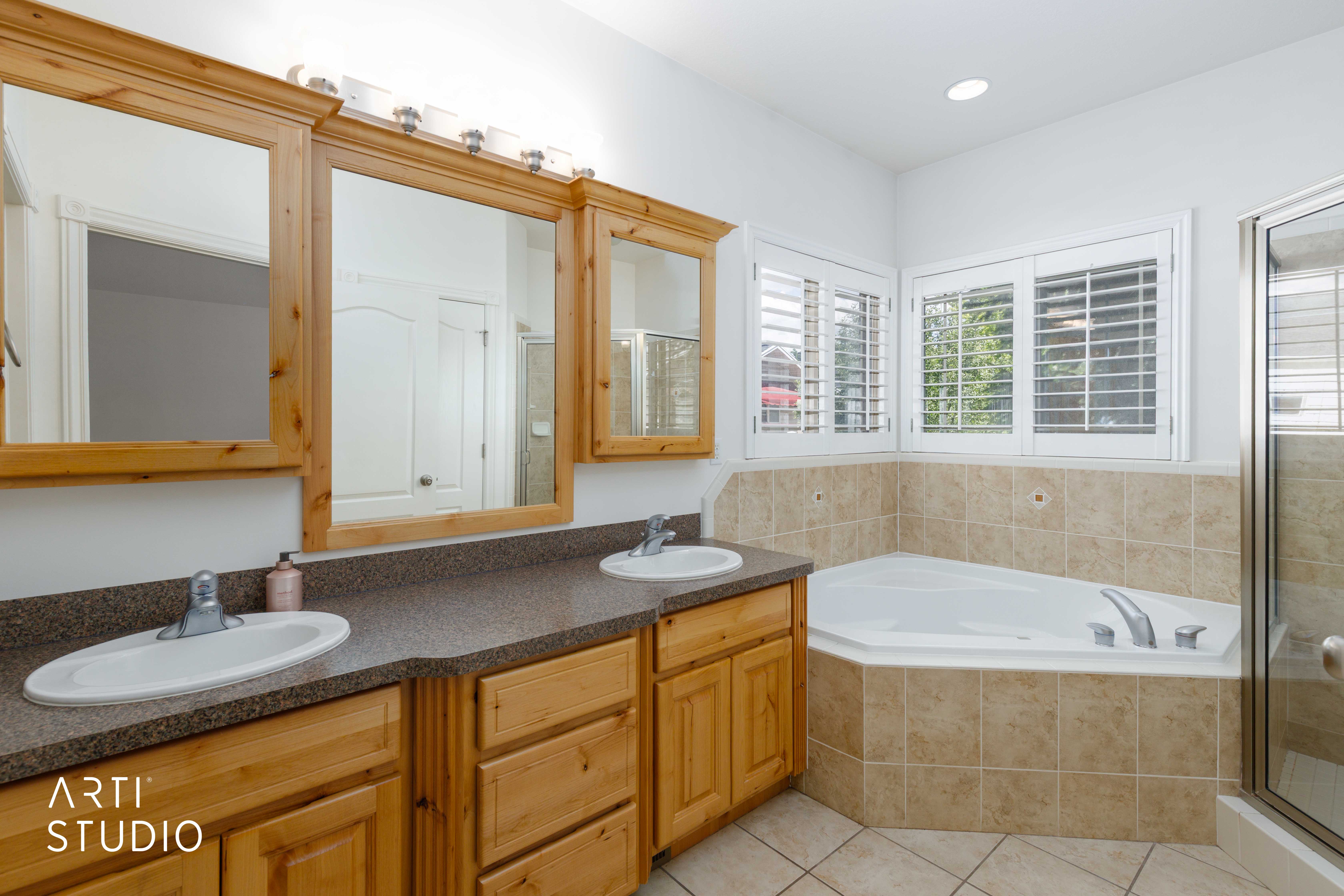 Bathroom featuring a corner soaking tub with tile surround, a double vanity with wood cabinetry, and plantation shutters