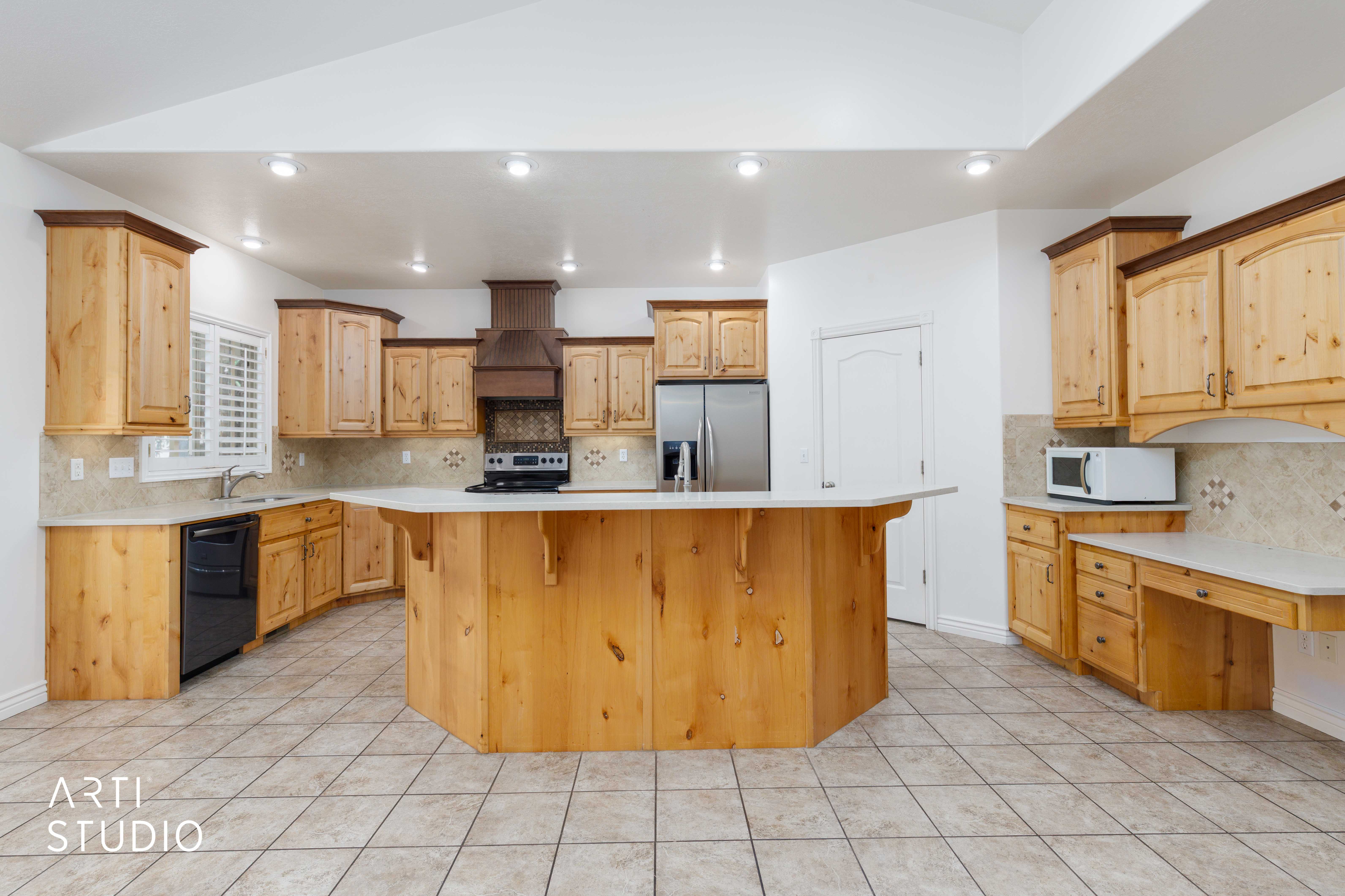 Spacious kitchen featuring a central island, light wood cabinetry with dark crown molding, tile flooring, and light countertops