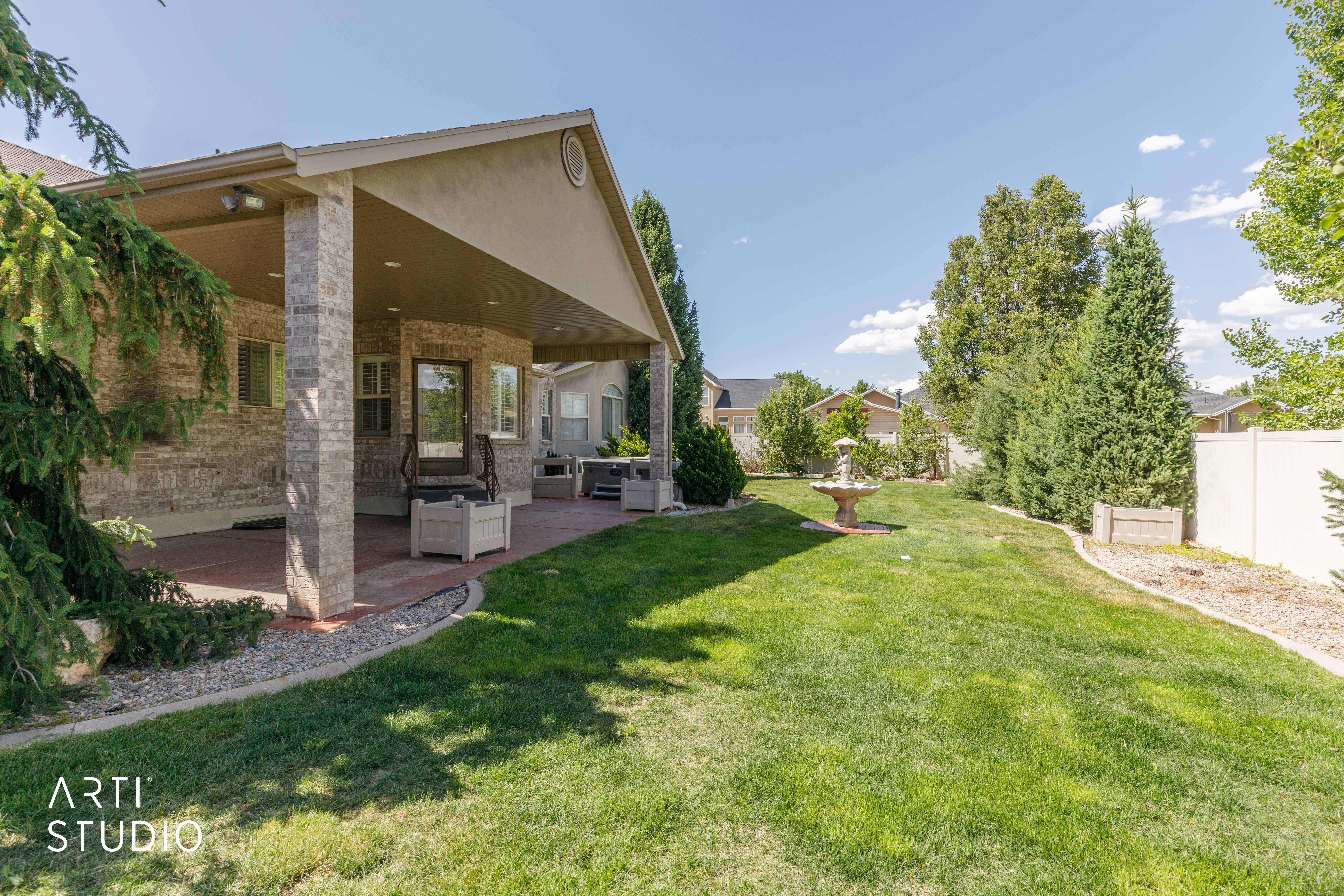 Expansive backyard featuring a covered patio with stone-clad pillars, a brick-patterned patio surface, and a decorative water fountain