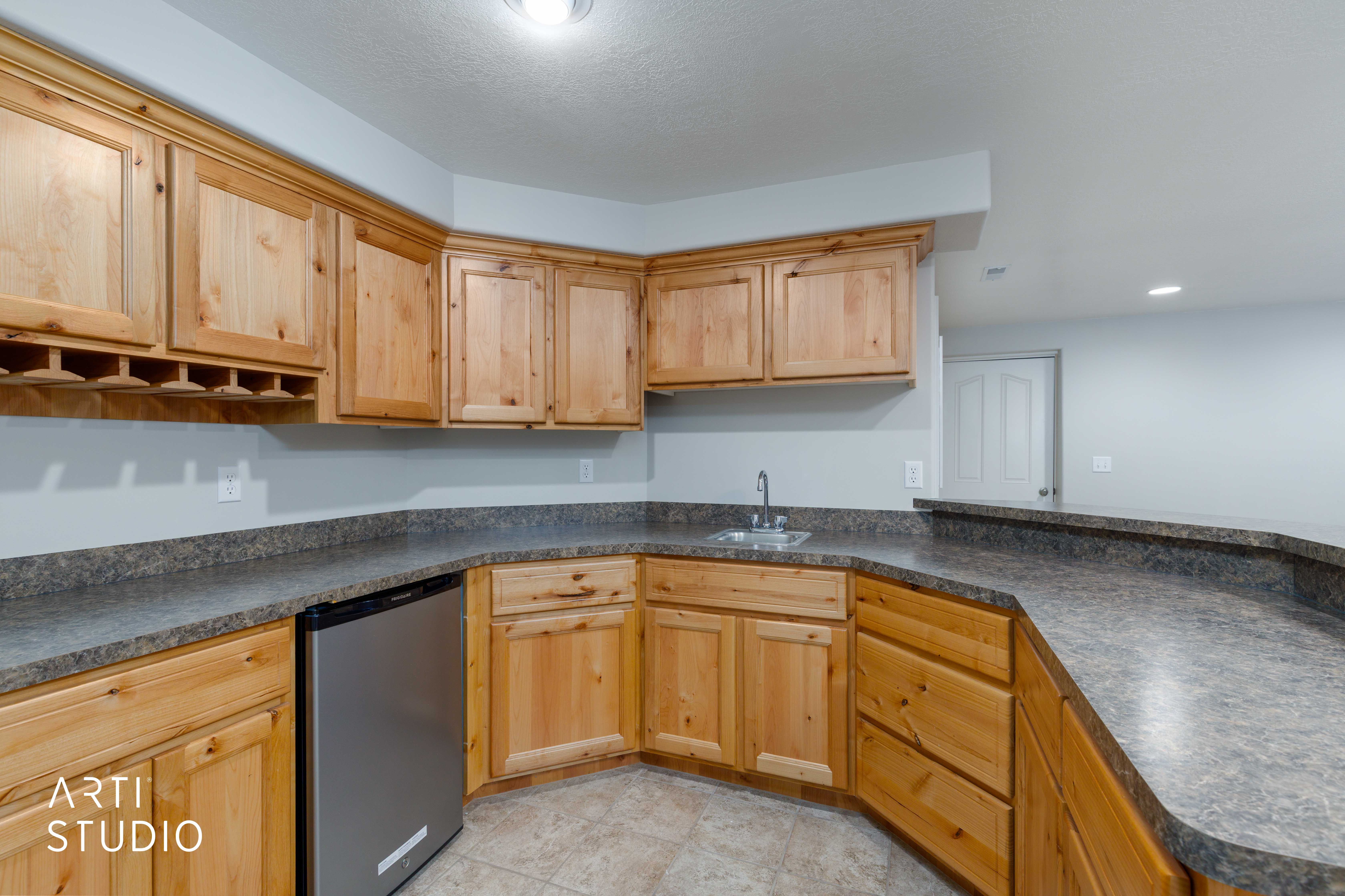 Kitchenette featuring light wood cabinetry, a stainless steel beverage refrigerator, a stainless steel sink with a chrome faucet, and speckled gray countertops