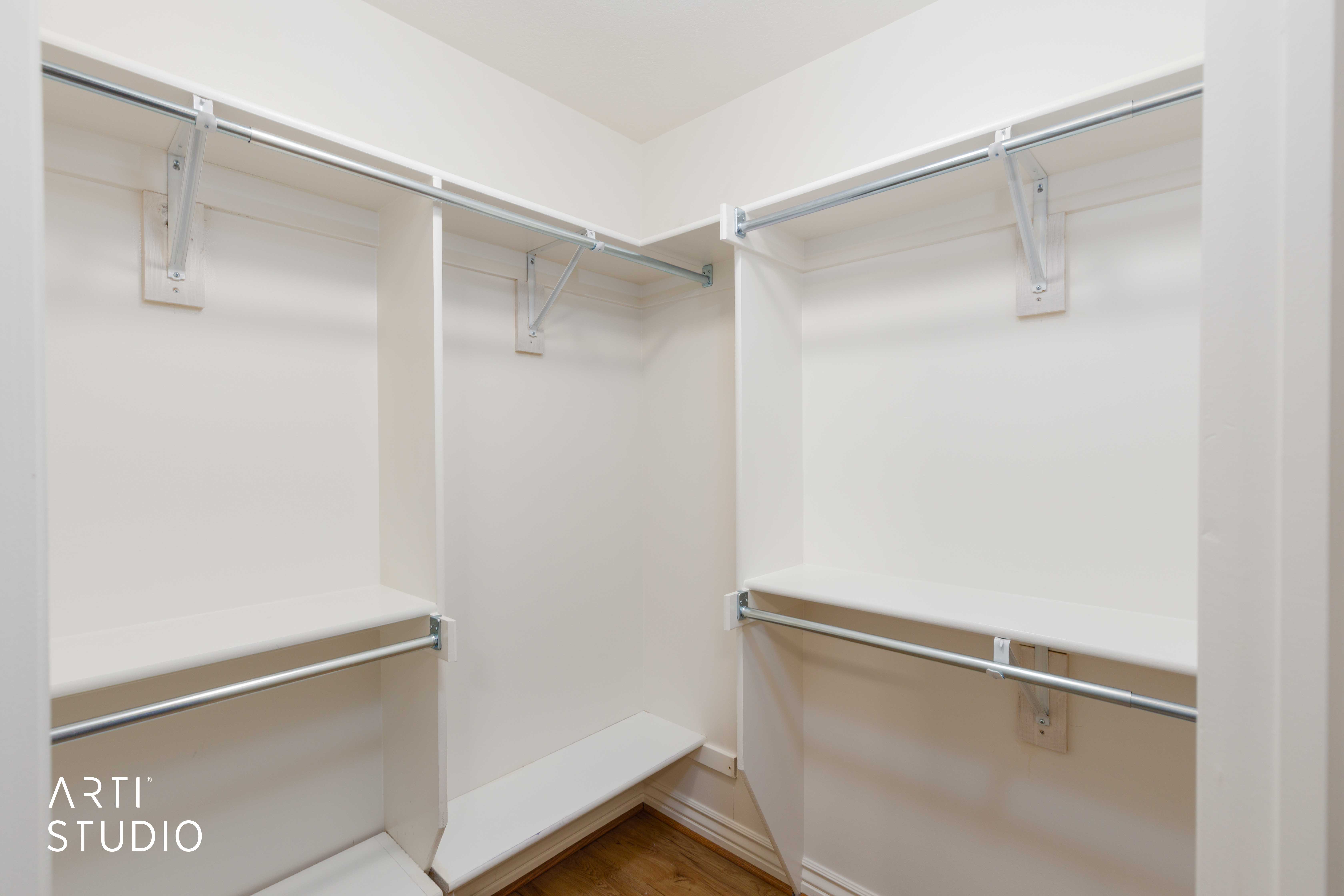 Walk-in closet featuring white shelving, multiple hanging rods, and wood-finish flooring
