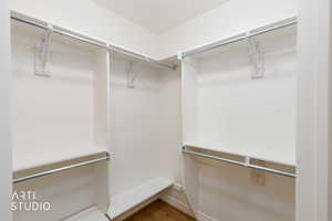 Walk-in closet featuring white shelving, multiple hanging rods, and wood-finish flooring