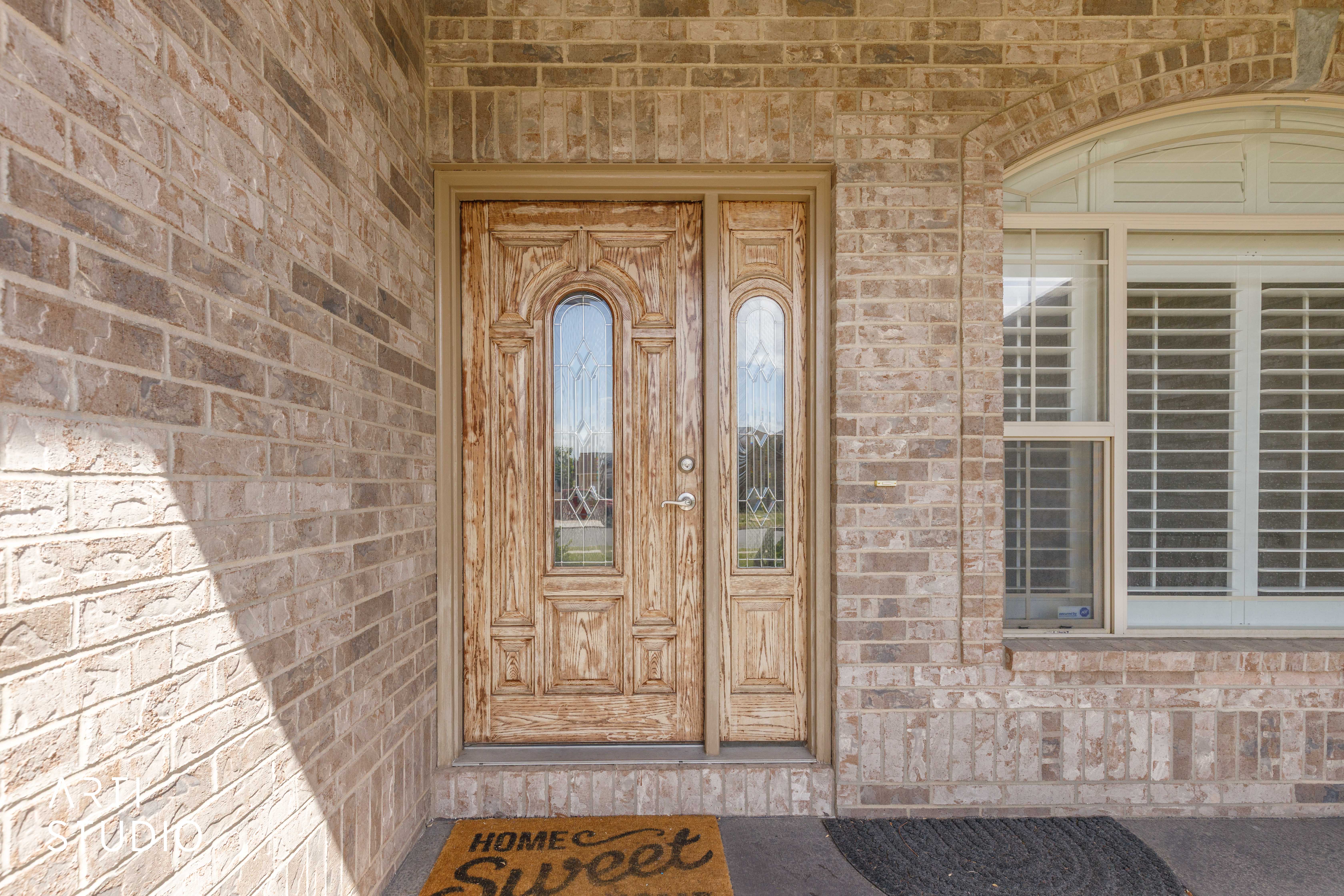Brick exterior featuring a paneled wood-finish door with decorative glass inserts and an arched transom window