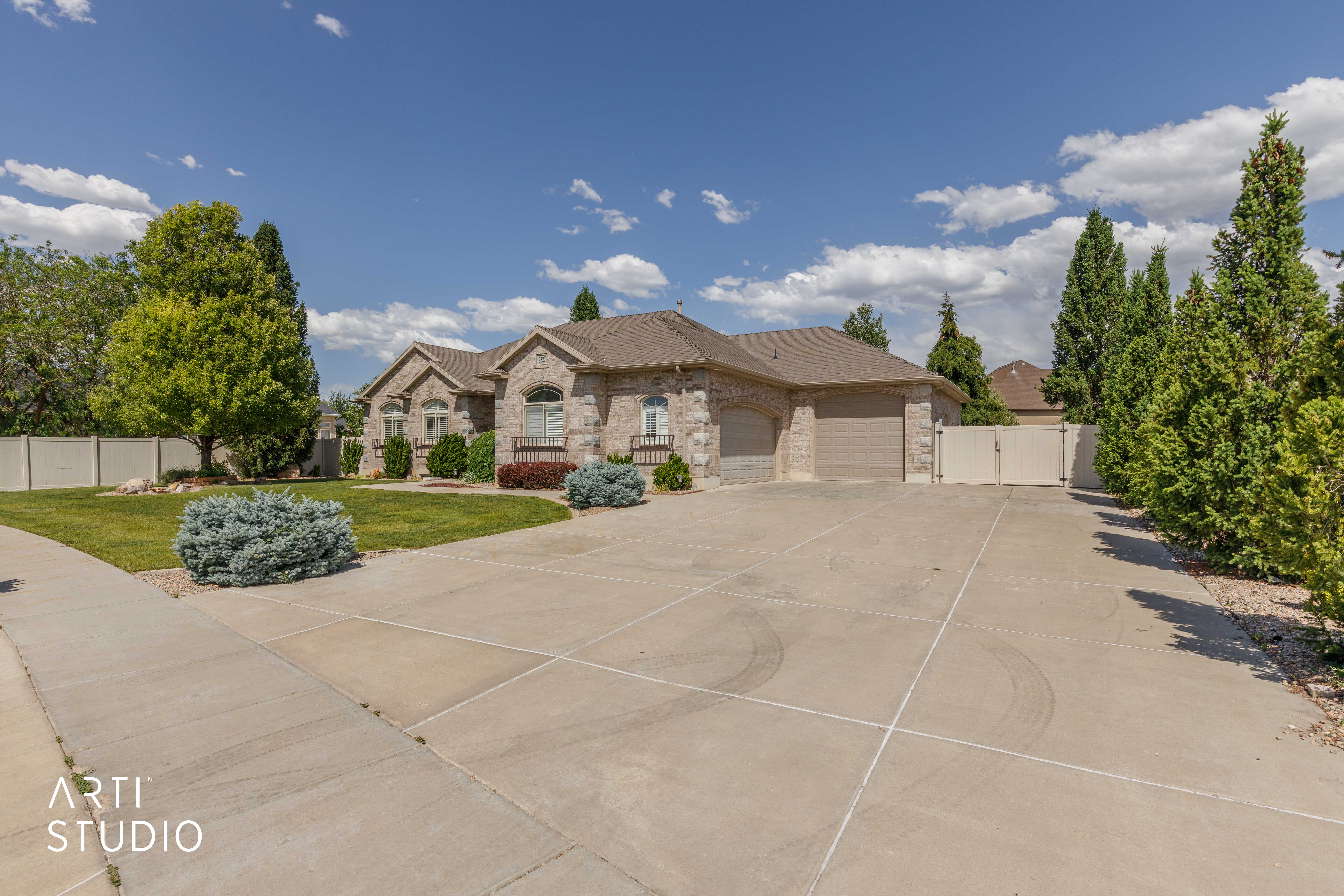 Stone facade residence featuring a multi-car garage, concrete driveway, and mature landscaping