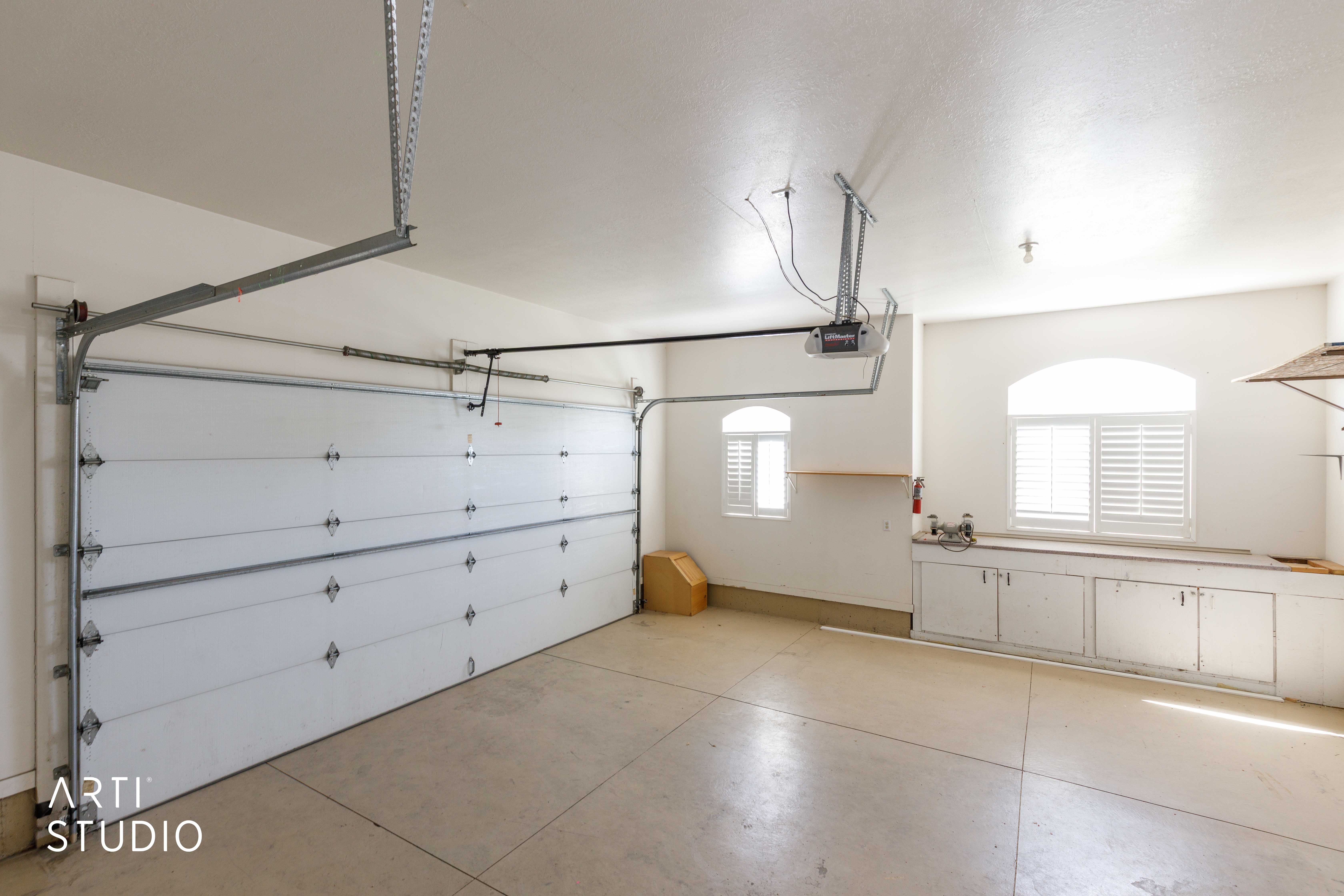 Spacious garage featuring a two-car overhead door, built-in cabinetry, two windows with plantation shutters, a utility sink, and concrete flooring