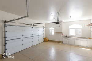 Spacious garage featuring a two-car overhead door, built-in cabinetry, two windows with plantation shutters, a utility sink, and concrete flooring