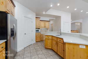 Kitchen featuring wood cabinetry, light-toned countertops, a stainless steel sink with a gooseneck faucet, recessed lighting, and tiled flooring