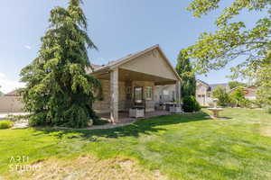 Expansive backyard featuring a covered patio with brick columns, a decorative fountain, and mature landscaping including a large evergreen tree