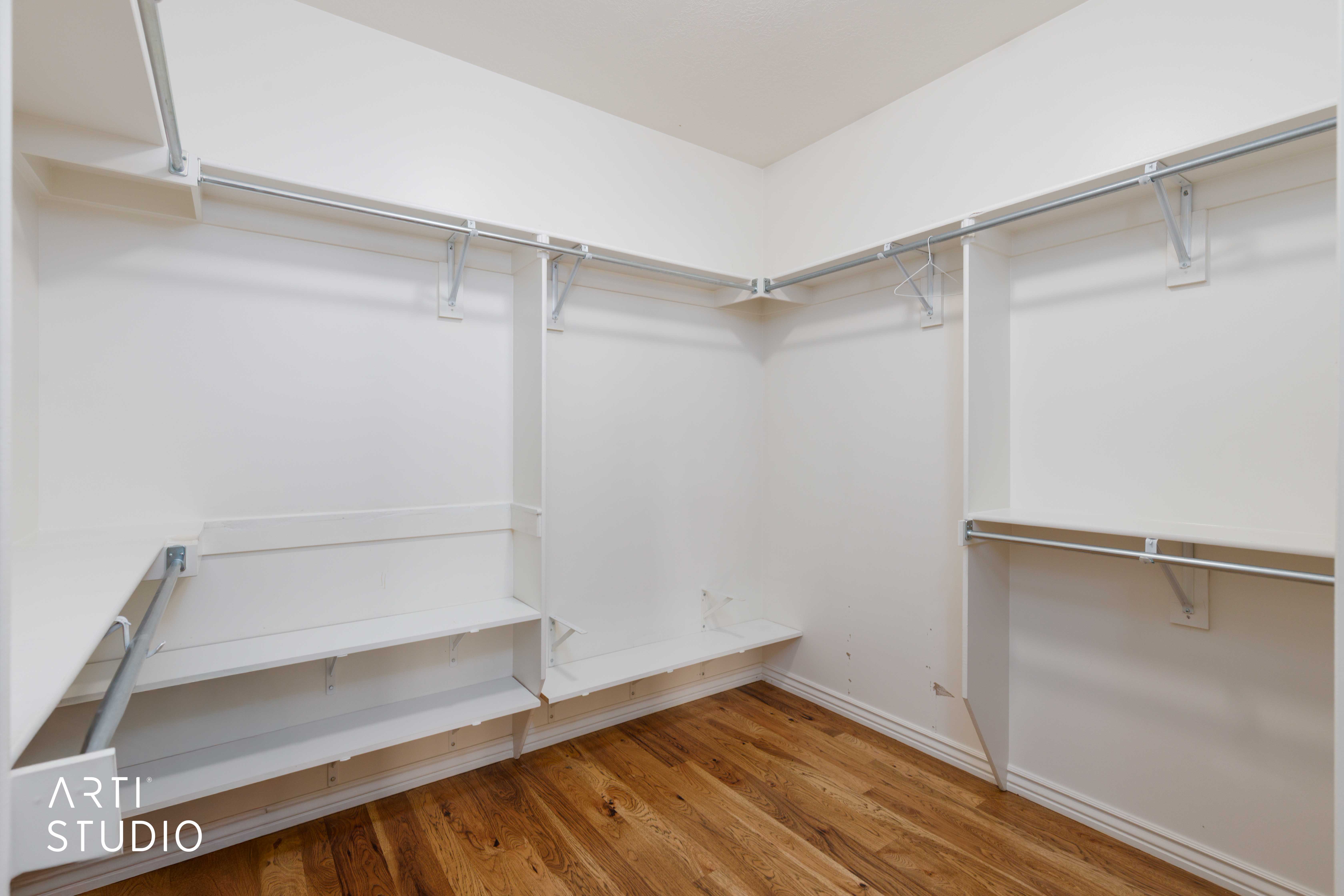 Spacious walk-in closet featuring wood-finish flooring, white walls, multiple shelving units, and metal hanging rods