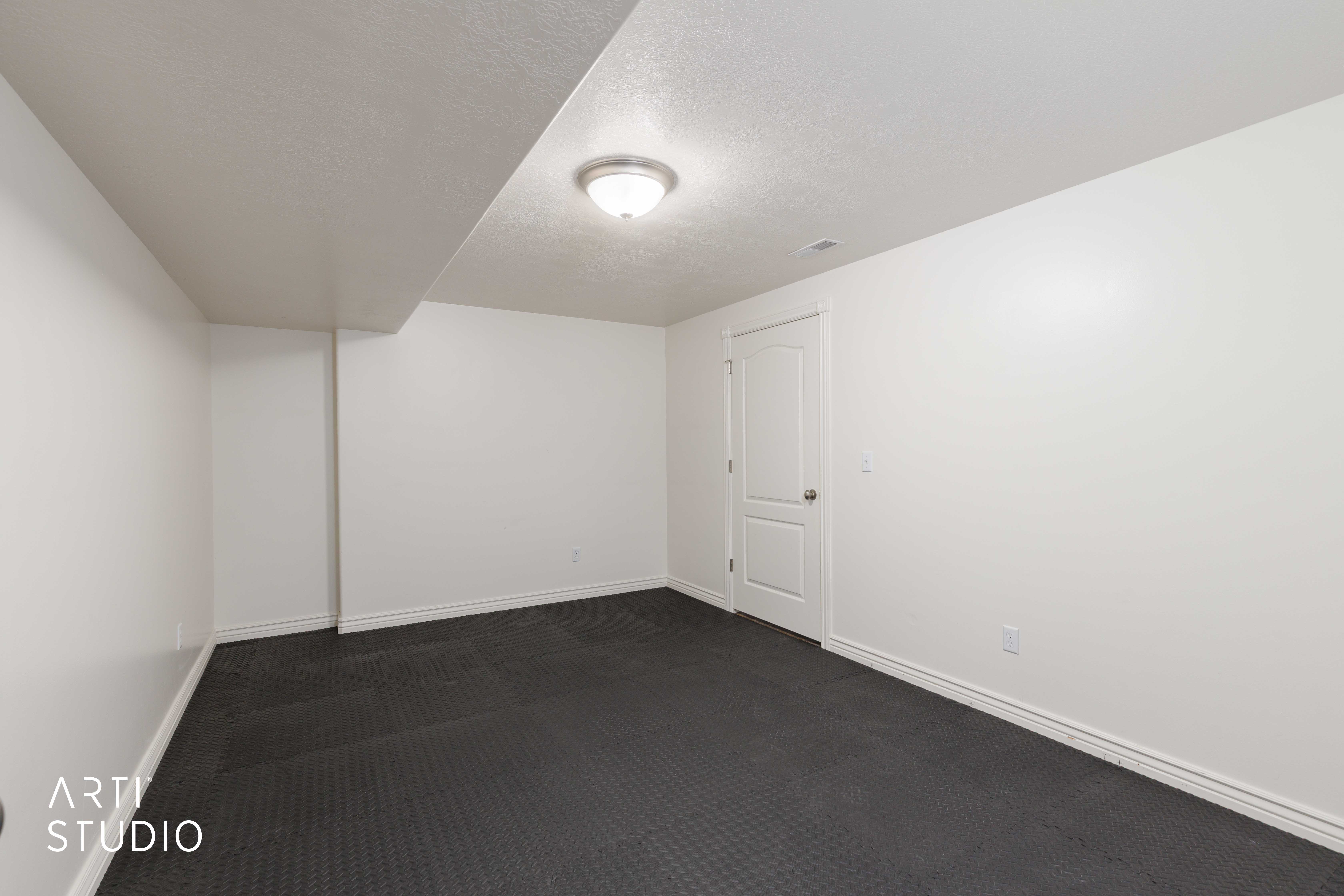 Spacious room featuring dark textured flooring, crisp white walls, white trim, a flush-mount ceiling light fixture, and a paneled interior door