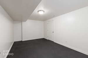 Spacious room featuring dark textured flooring, crisp white walls, white trim, a flush-mount ceiling light fixture, and a paneled interior door