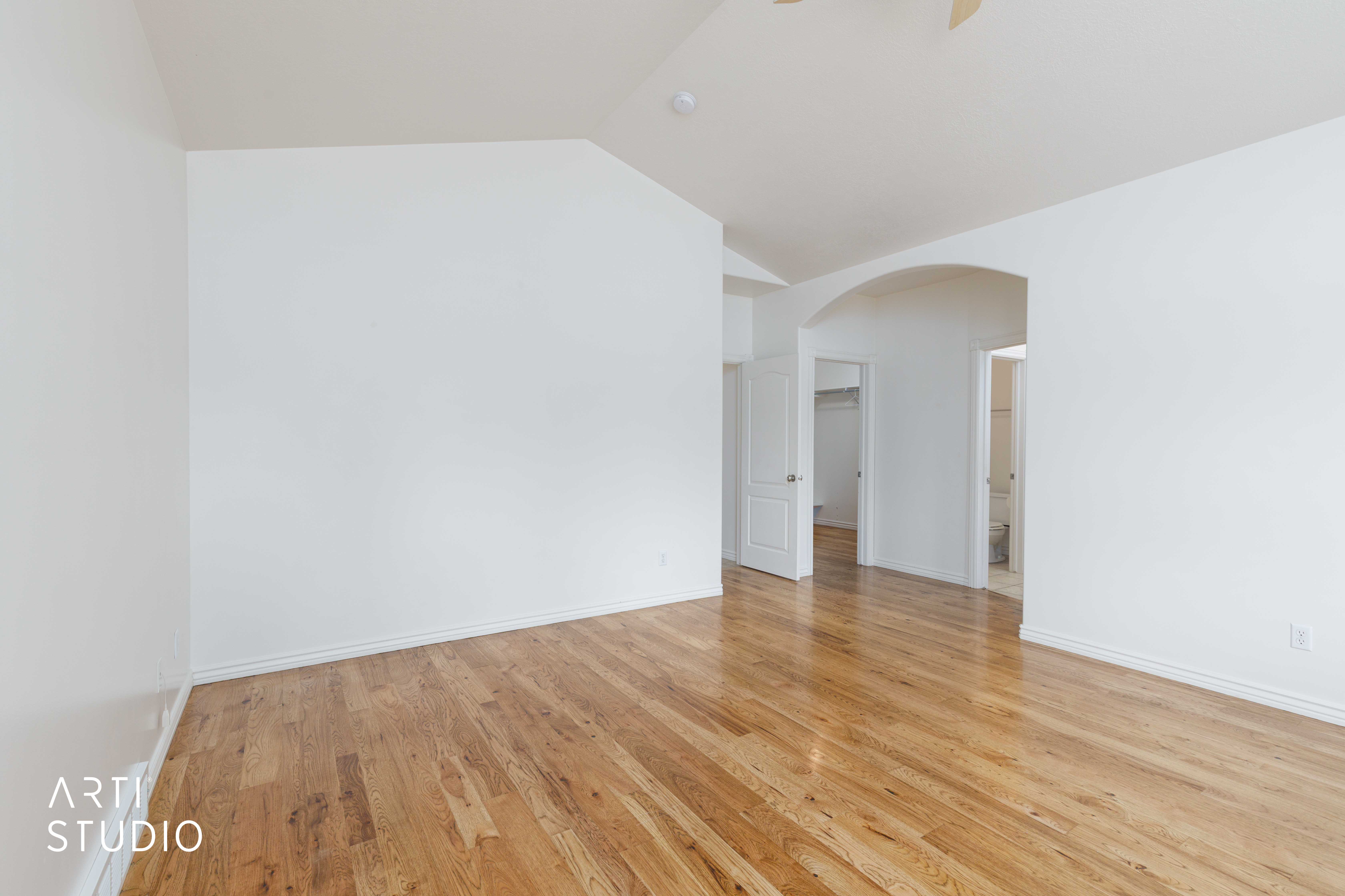 Spacious room featuring wood flooring, vaulted ceiling, white baseboards, and a wide arched doorway