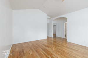 Spacious room featuring wood flooring, vaulted ceiling, white baseboards, and a wide arched doorway