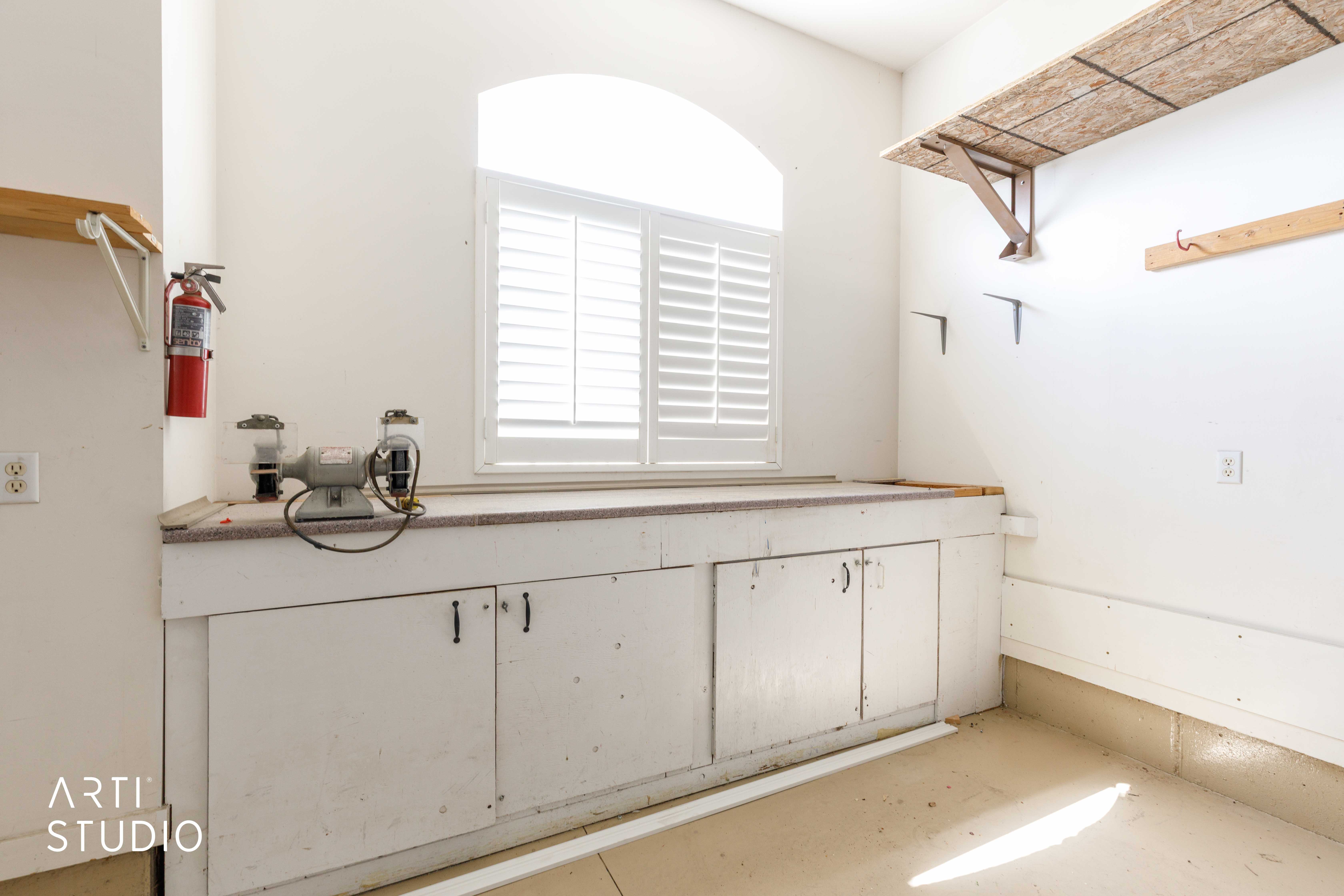 Built-in workbench with storage cabinetry, featuring a countertop and an arched window with plantation shutters