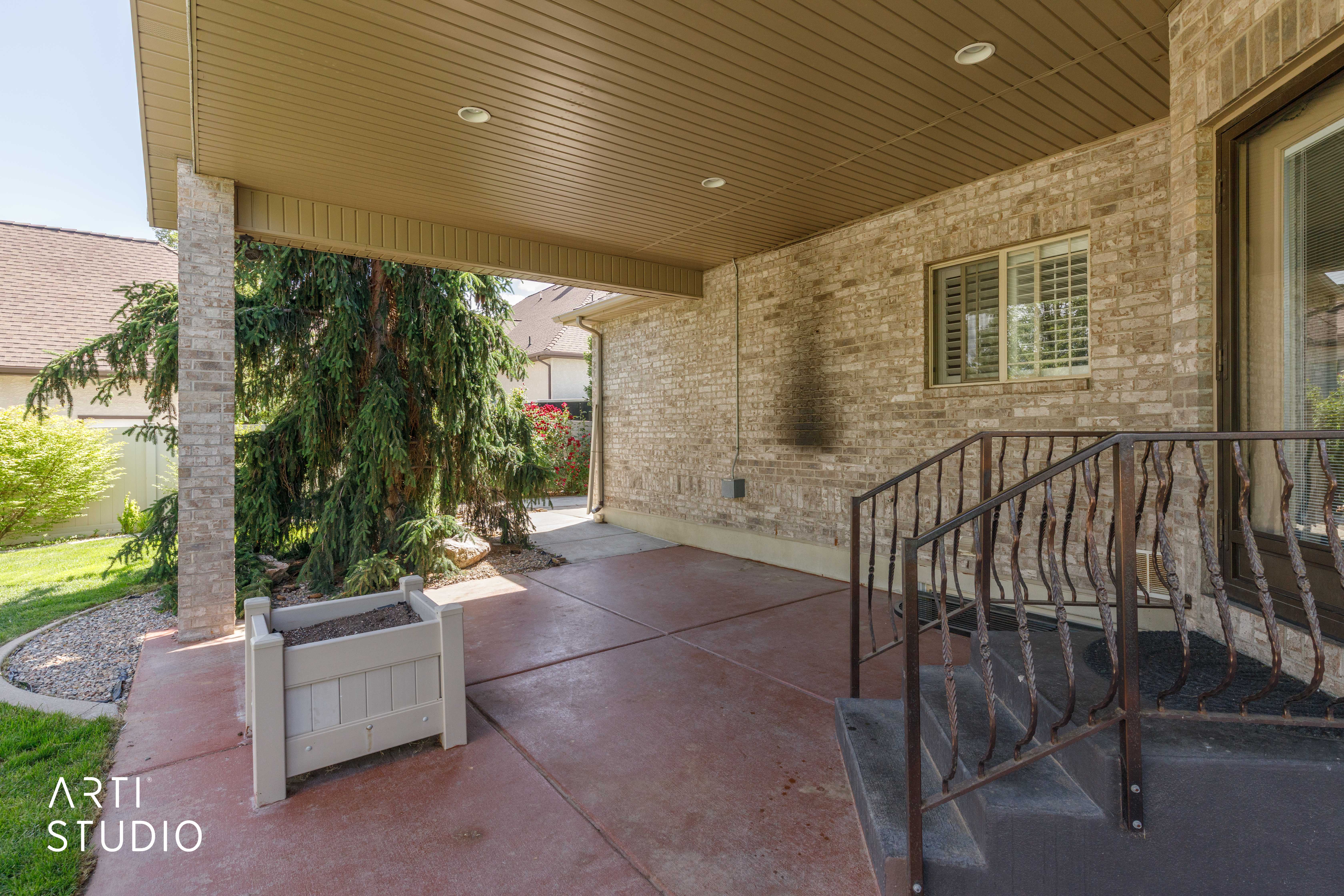 Covered patio featuring a brick facade, stamped concrete flooring, and an ornamental metal railing