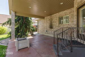 Covered patio featuring a brick facade, stamped concrete flooring, and an ornamental metal railing