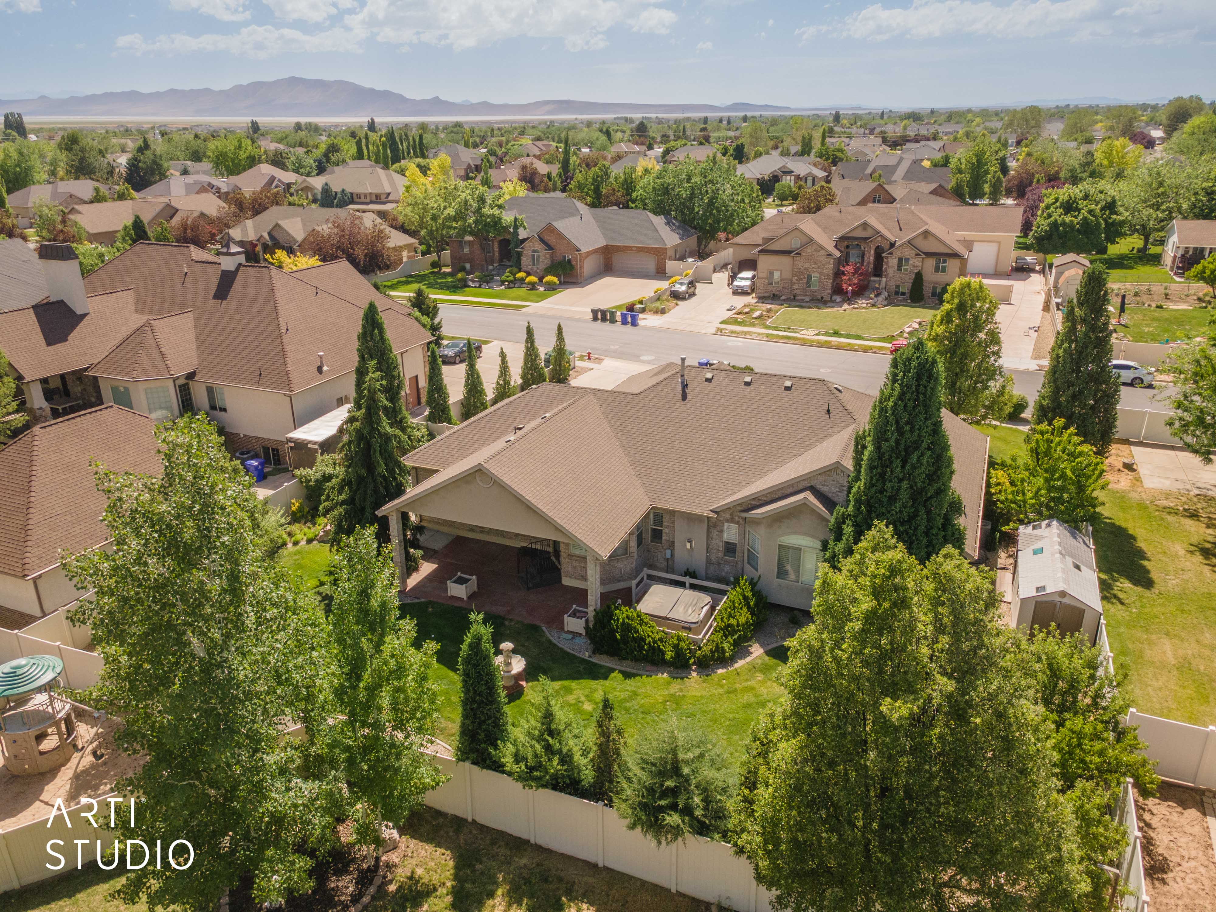 Expansive property featuring a covered patio, a manicured lawn, mature trees, and a storage shed