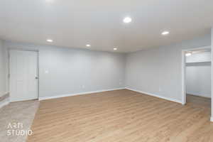 Spacious room featuring light wood-finish flooring, recessed lighting, neutral wall tones, and white baseboards