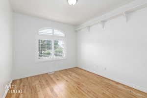 Bright interior space featuring wood-finish flooring, white walls, and an arched window with plantation shutters