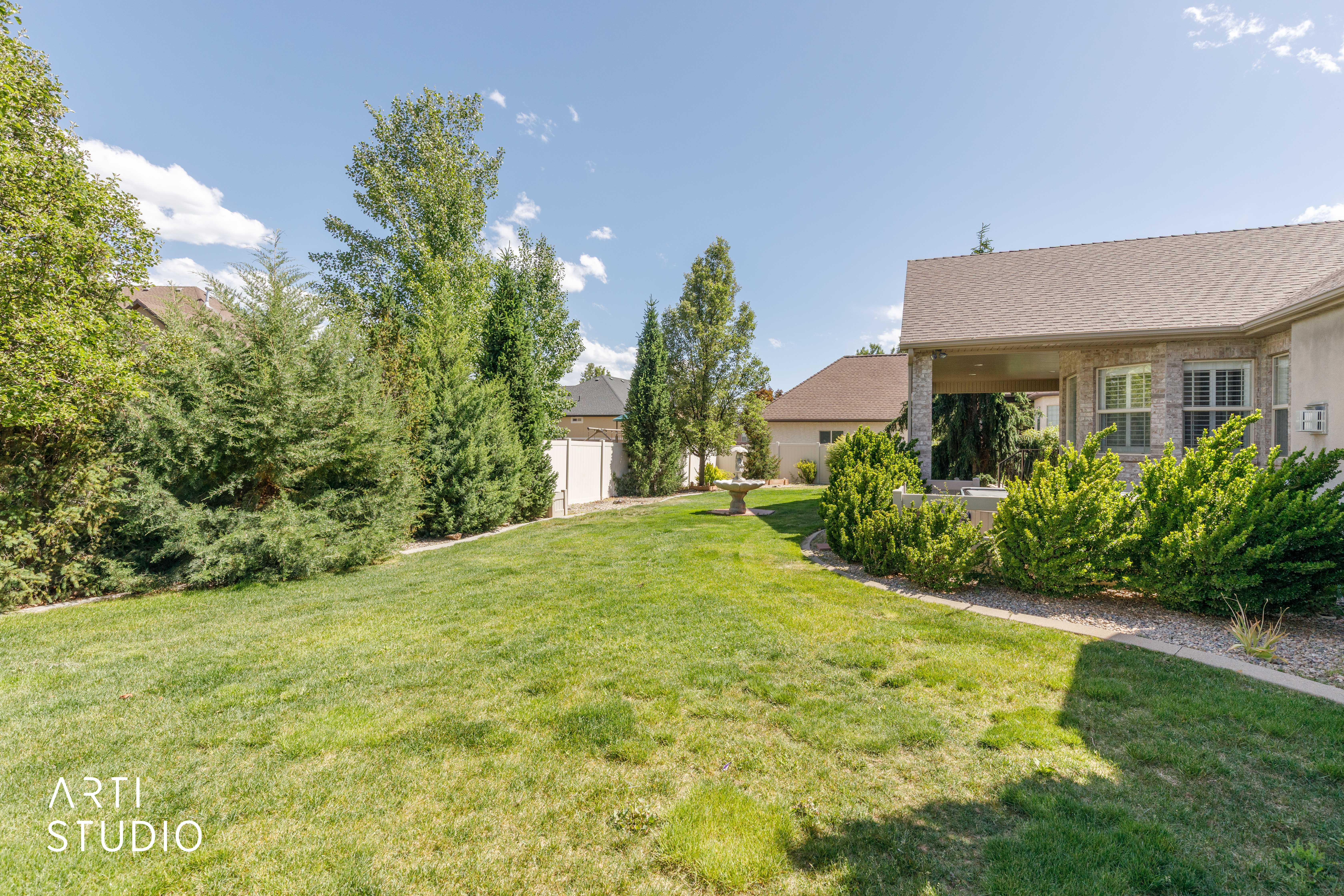 Expansive backyard featuring a manicured lawn, established landscaping, and a covered patio