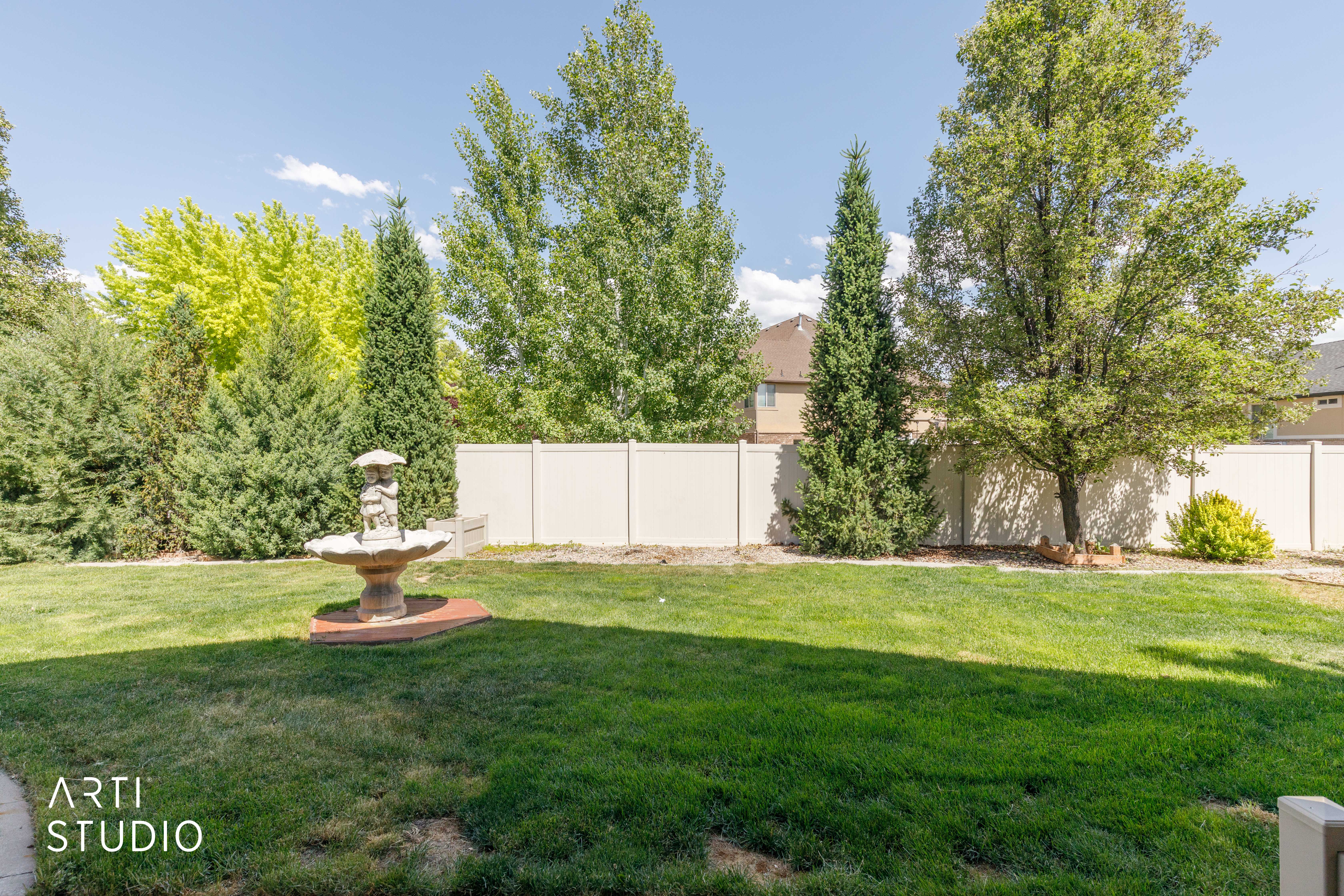 Expansive lawn area featuring a decorative garden fountain on a paver base, surrounded by mature trees and evergreen shrubs