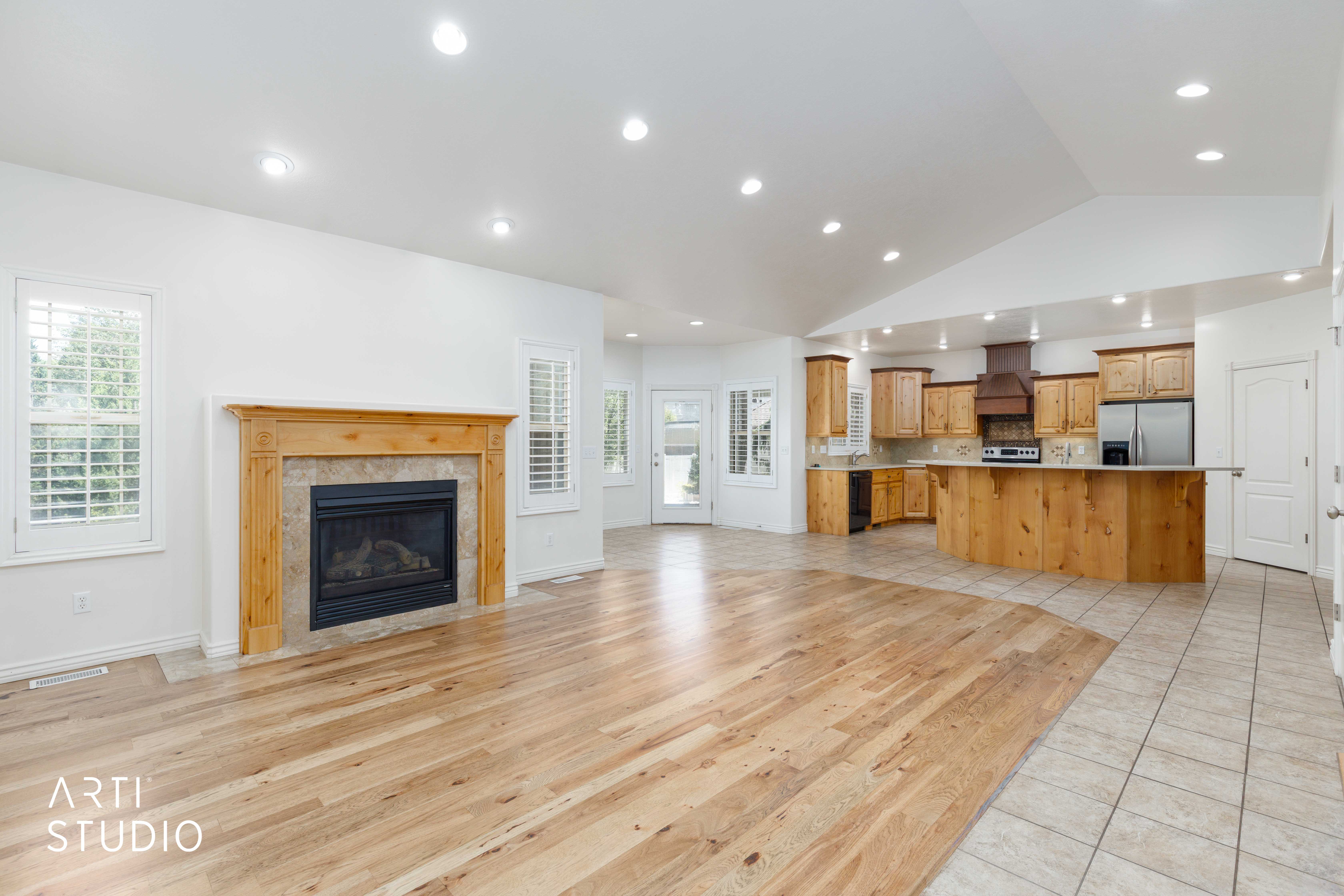 Open-concept living space featuring wood-finish flooring, a fireplace with a wood mantel and stone surround, and an adjacent kitchen with wood cabinetry and stainless steel appliances