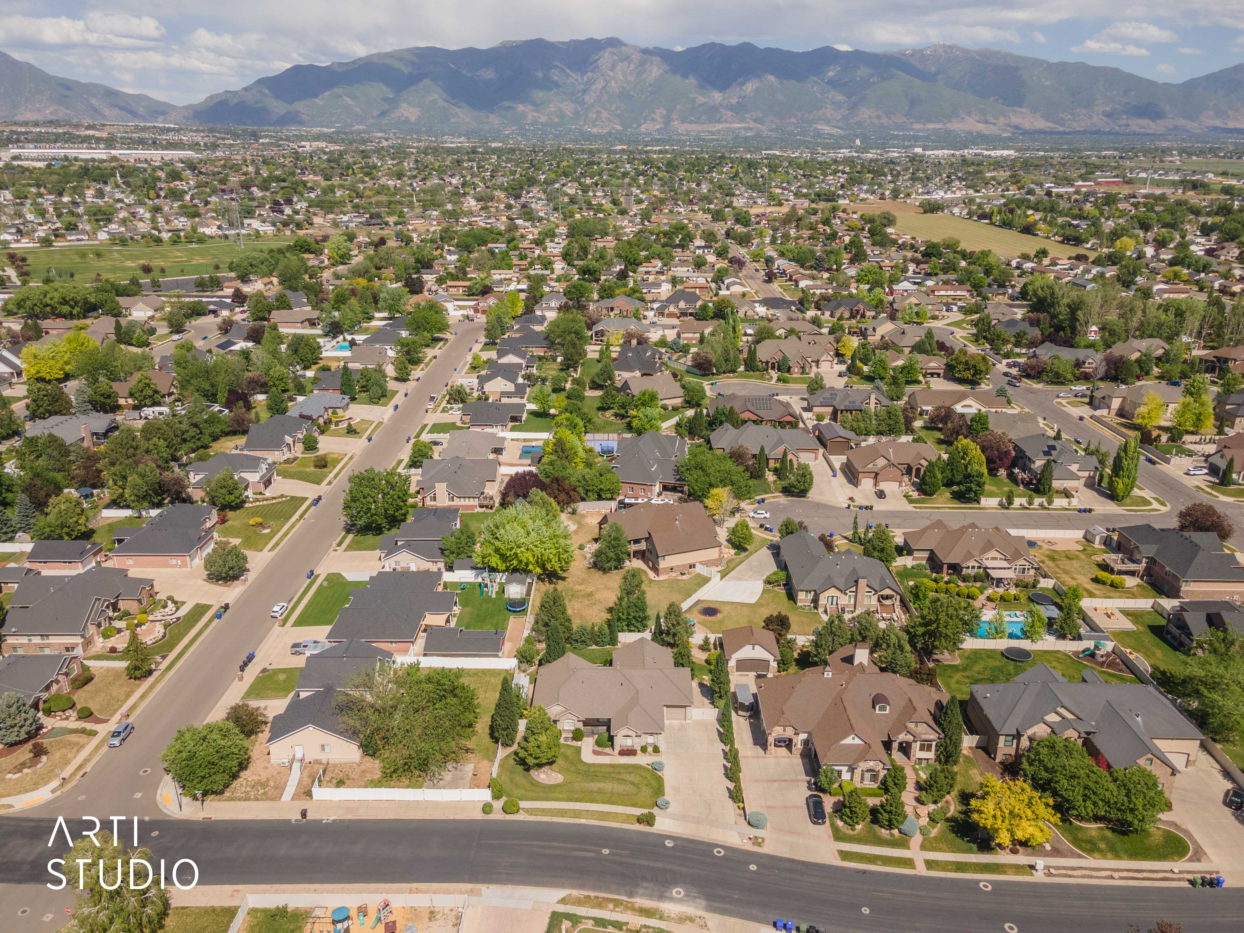 Expansive residential area with a mountain backdrop, featuring numerous single-family homes, mature trees, paved streets, and a mixture of residential and undeveloped land