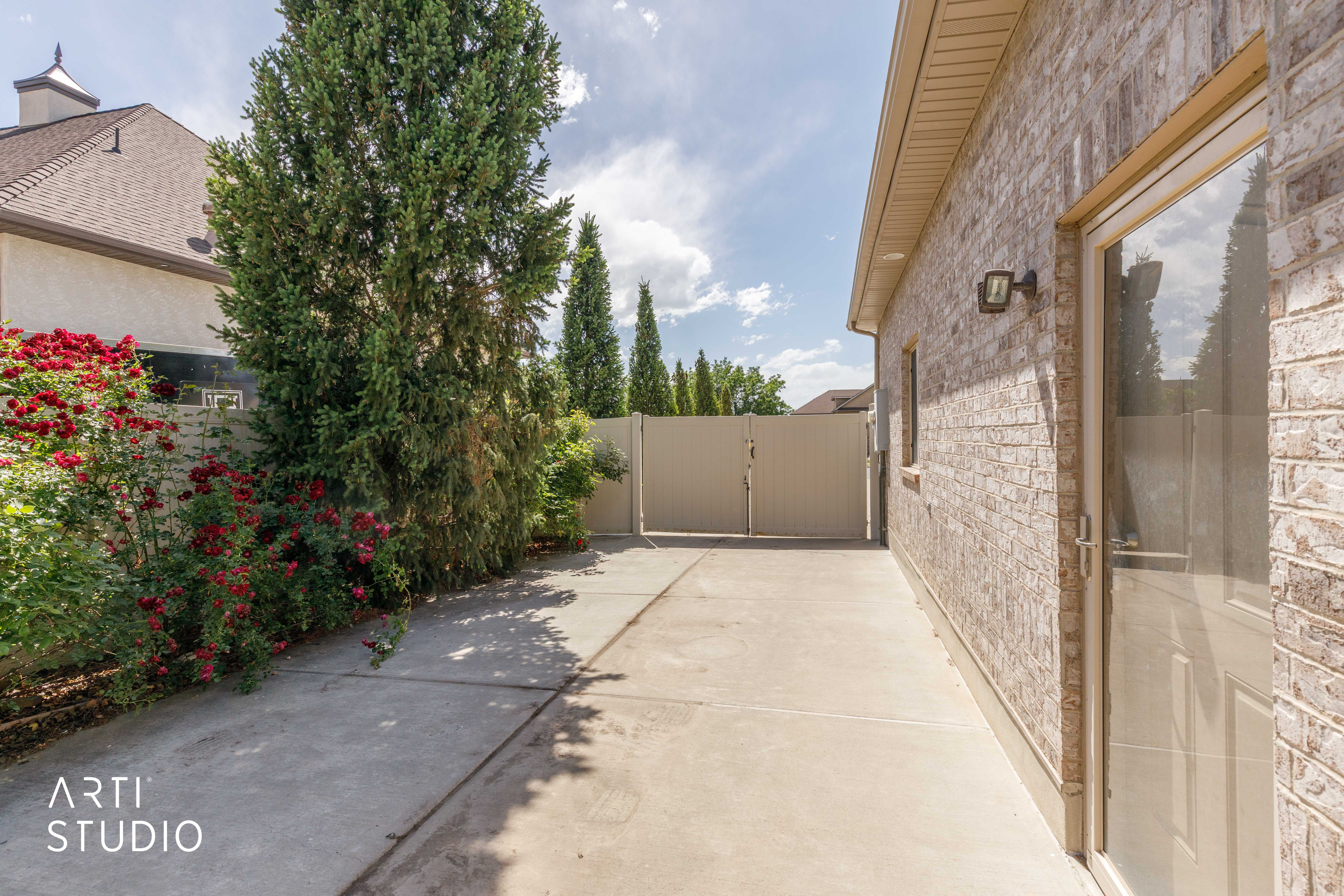 Side yard featuring a concrete pathway, mature evergreen trees, and a privacy fence