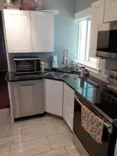 Modern kitchen featuring white shaker cabinetry, stainless steel appliances, dark countertops, a double basin sink, and tile flooring