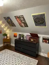 Sloped ceiling room featuring wood-finish flooring, light gray wall paint, and white baseboards