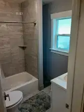 Bathroom featuring a white bathtub, grey wall tiling, and a white vanity with an integrated sink