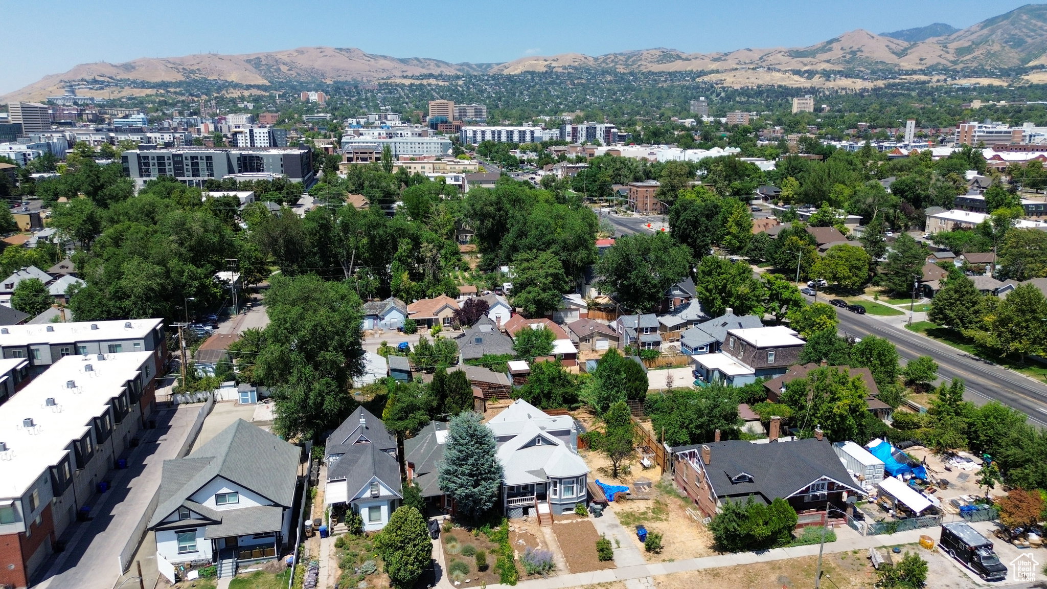 Aerial perspective showcasing an urban neighborhood with established trees, a distant cityscape, and a mountainous backdrop